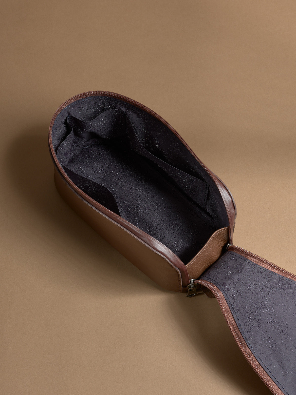 Open brown Capra Leather Toiletry Bag showing the water-resistant lining with moisture droplets.