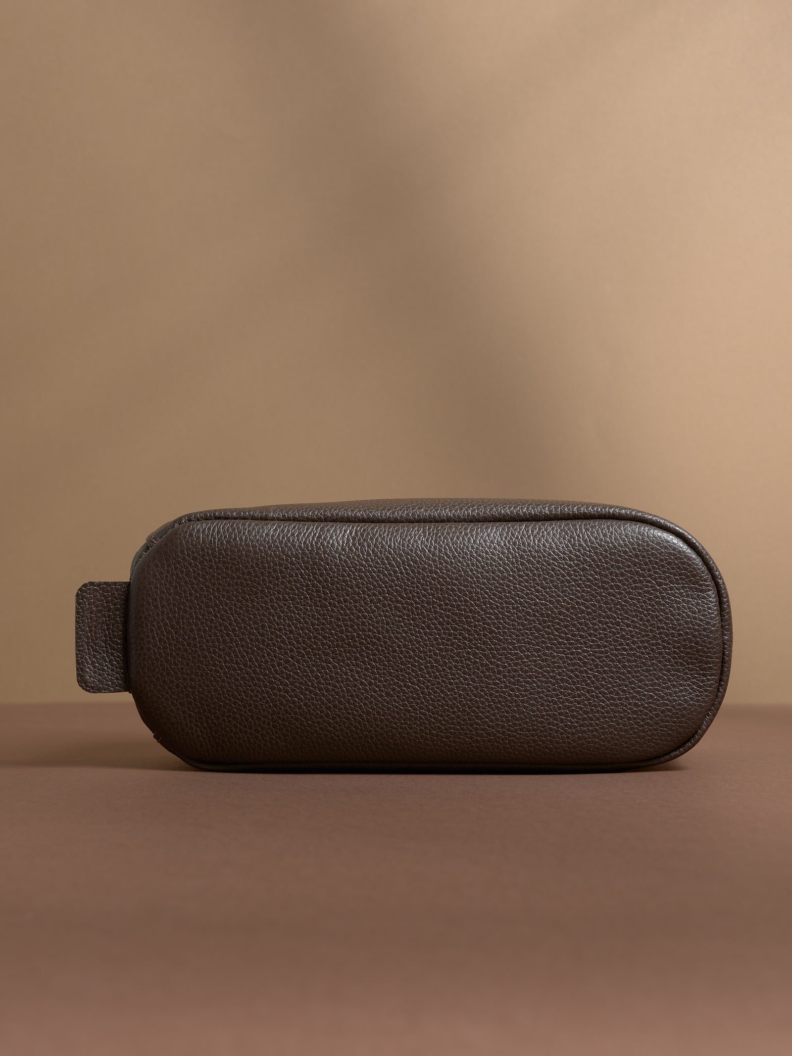 Bottom view of the dark brown Capra Leather Toiletry Bag, showing the rounded base and loop.