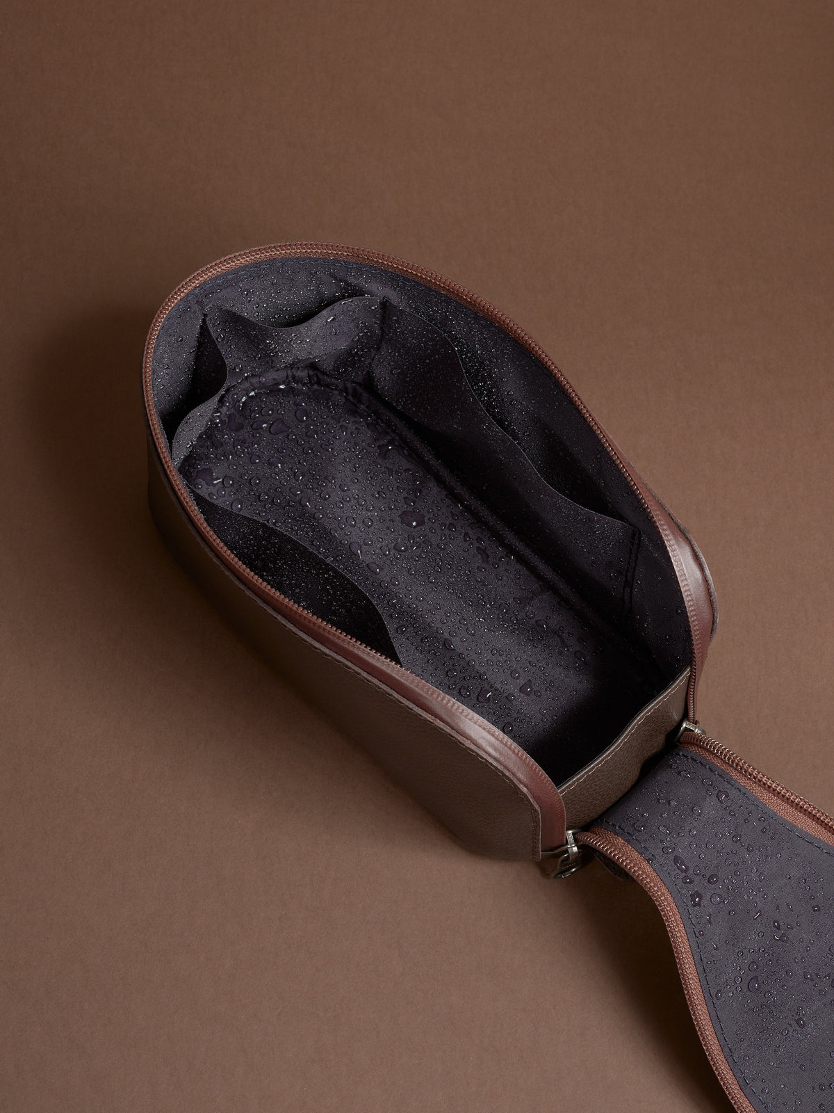 Open dark brown Capra Leather Toiletry Bag showing the water-resistant lining with moisture.
