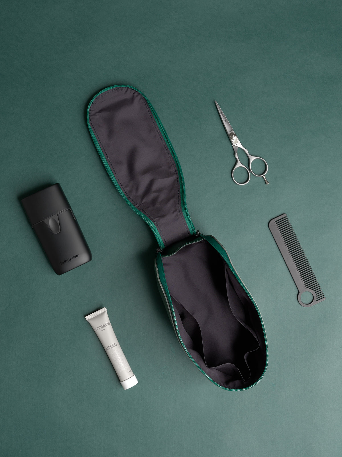 Open deep green Capra Leather Toiletry Bag laid out with a razor, comb, and grooming products.