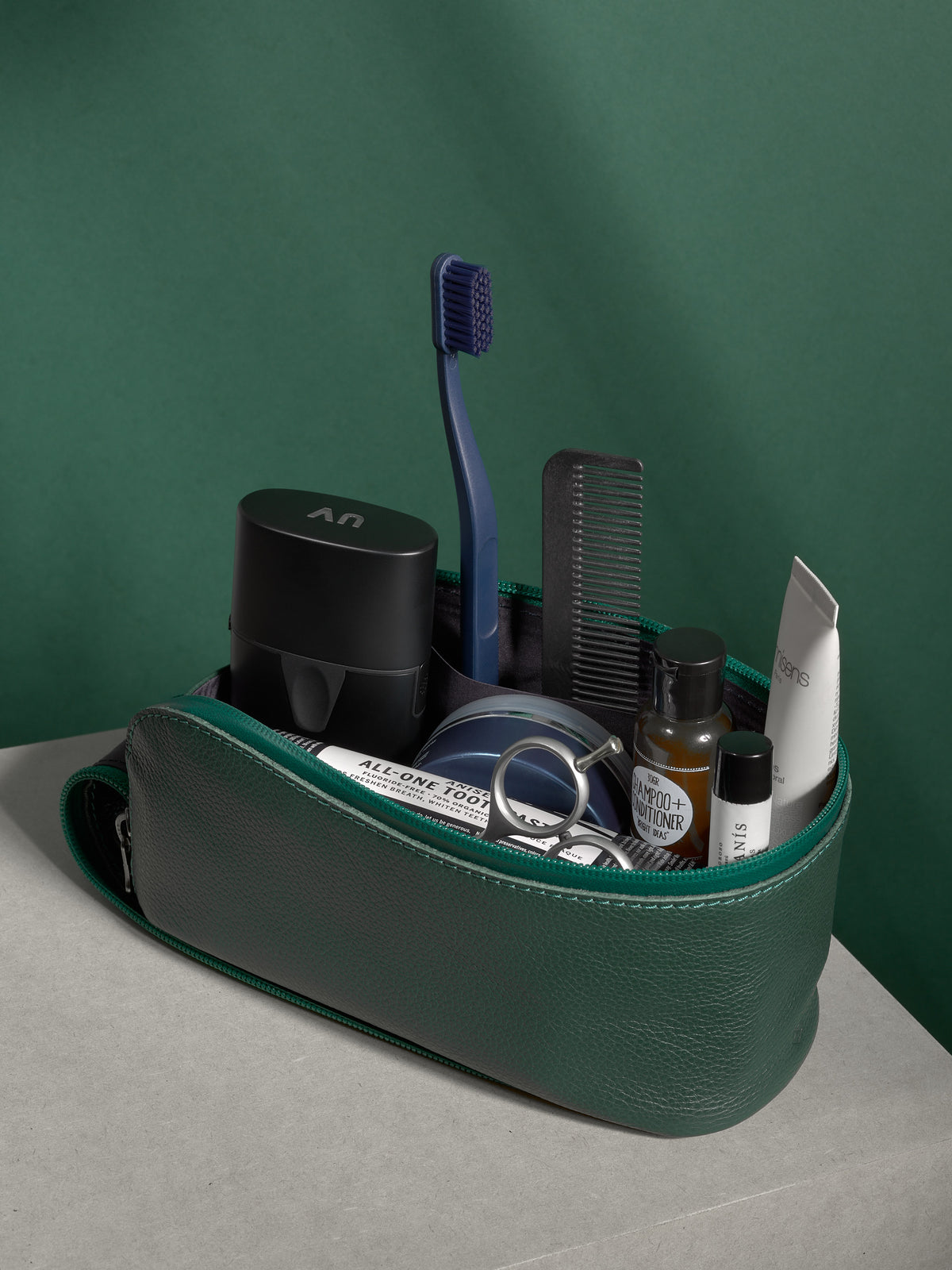 Open green Capra Leather Toiletry Bag packed full of men's grooming and travel essentials.