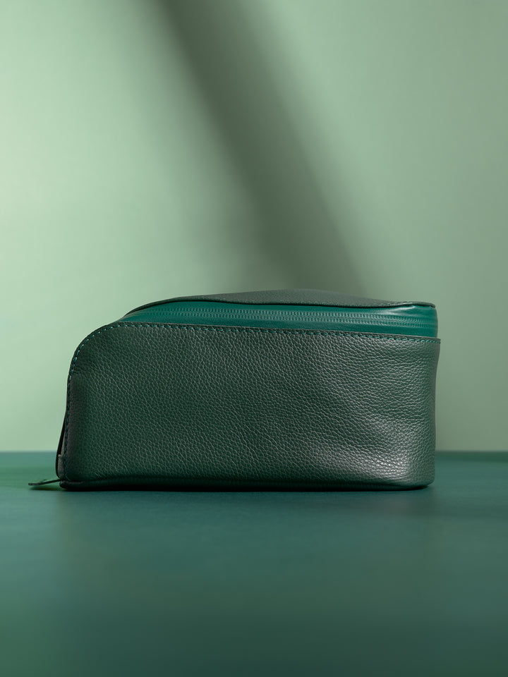 Side profile of the closed dark green Capra Leather Toiletry Bag, showing its elegant curve.