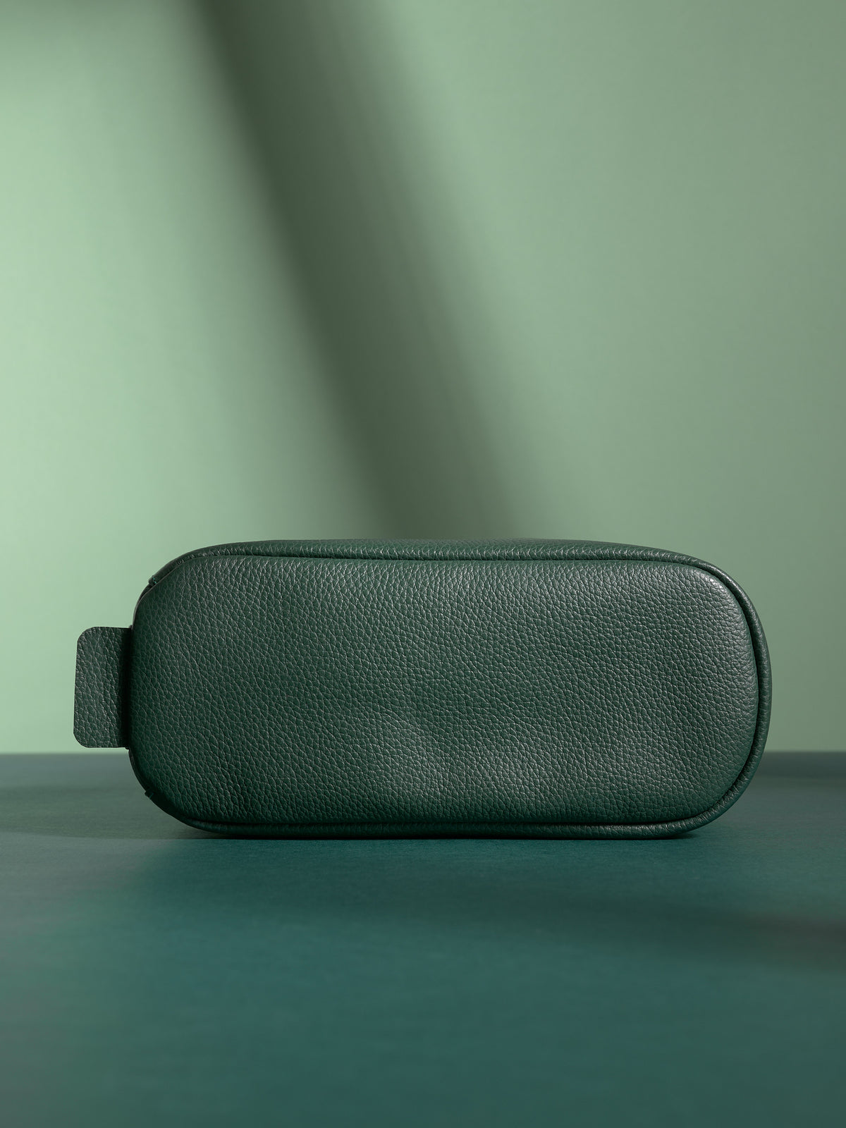 Bottom view of the deep green Capra Leather Toiletry Bag showing the base and leather loop.