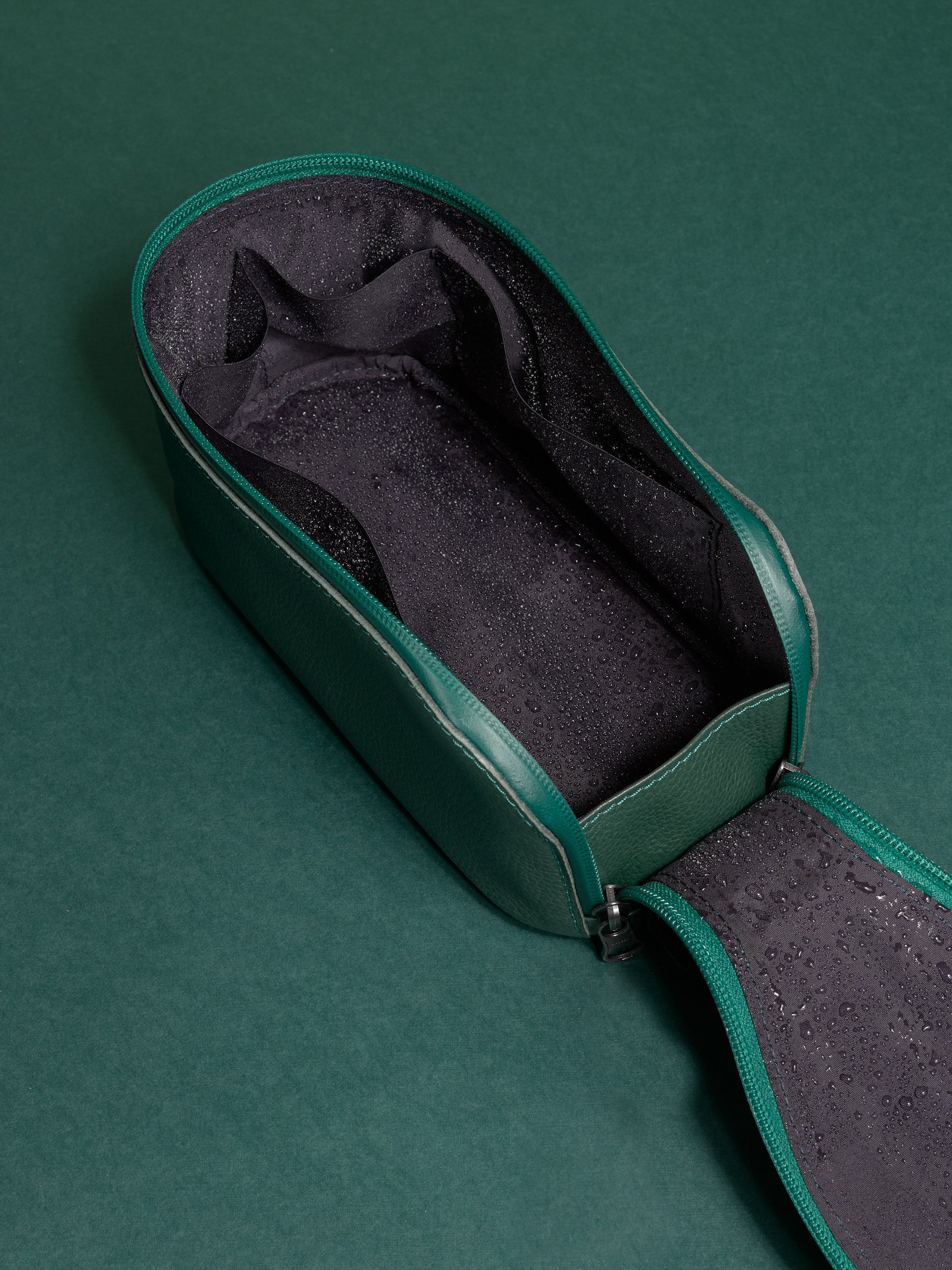 Open green Capra Leather Toiletry Bag interior showing the dark, water-resistant lining with moisture.