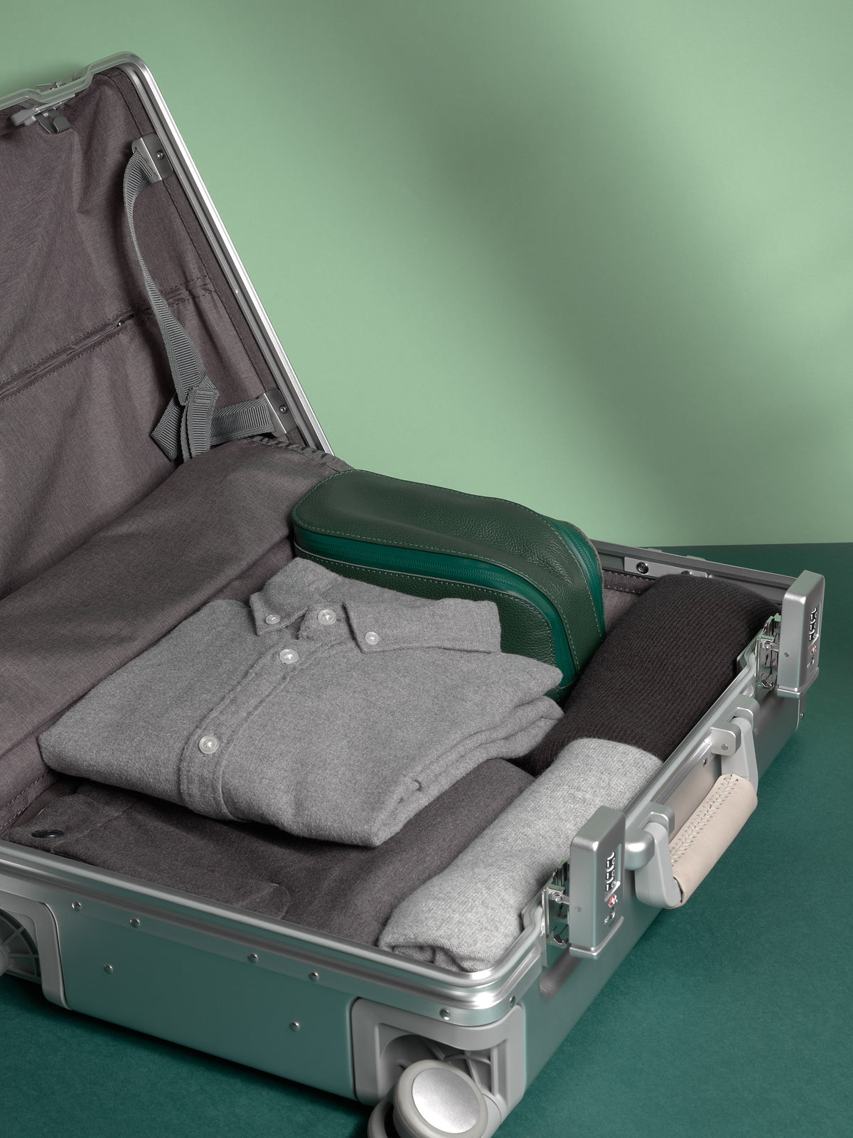 Green Capra Leather Toiletry Bag packed inside a silver suitcase with neatly folded travel clothes