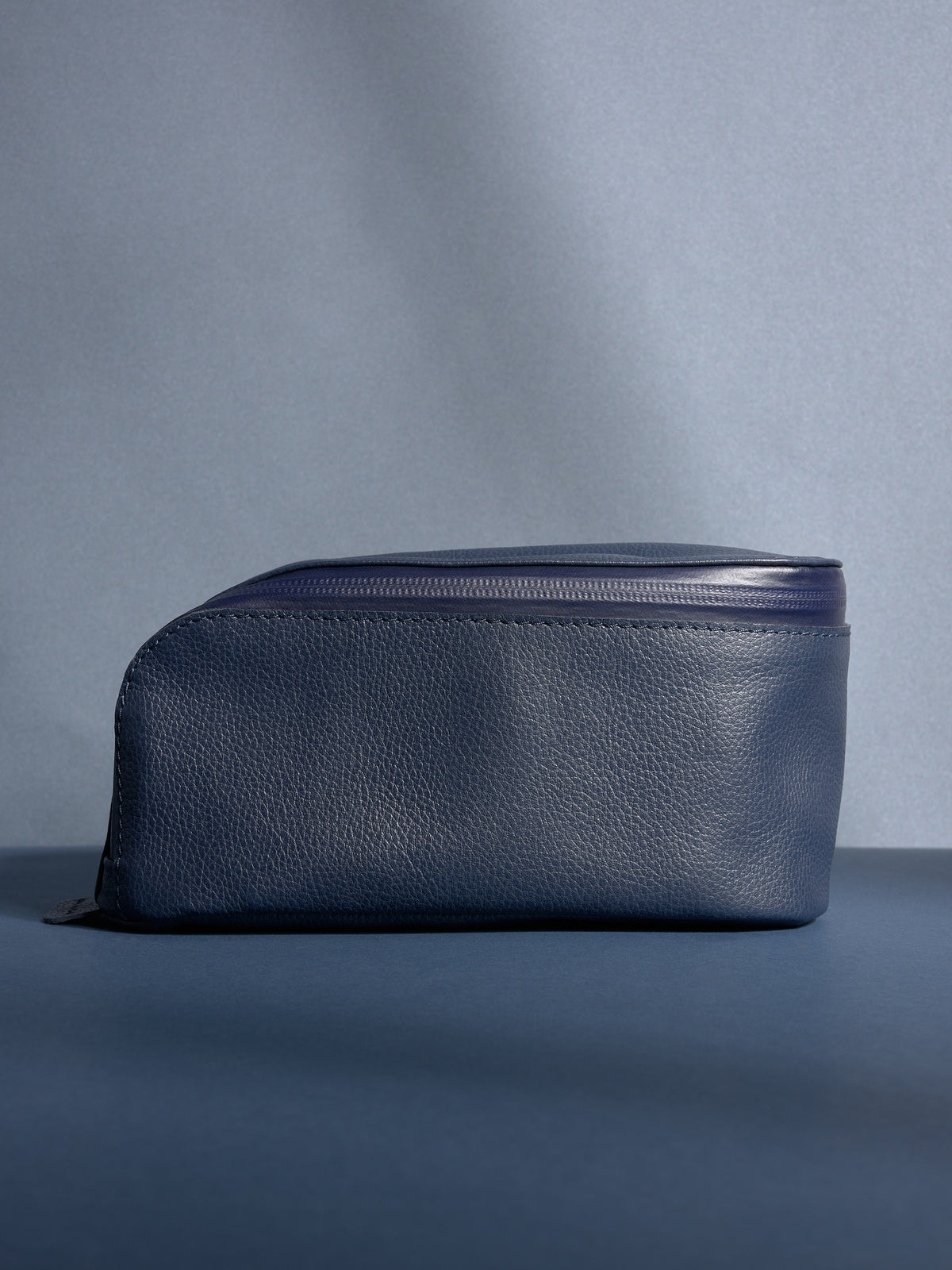 Full side view of the personalized navy Capra leather toiletry bag, showcasing its sleek profile.