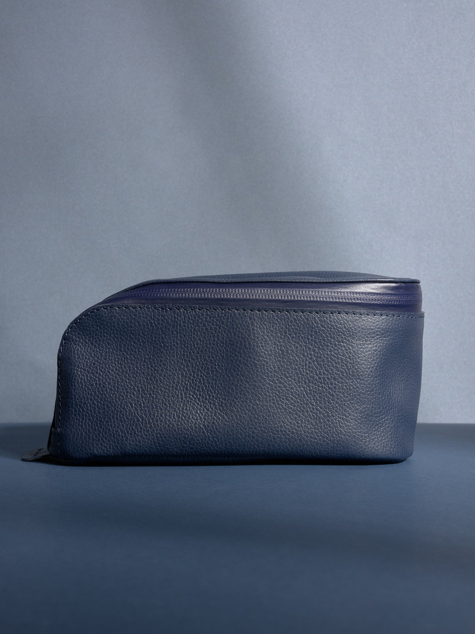 Full side view of the personalized navy Capra leather toiletry bag, showcasing its sleek profile.