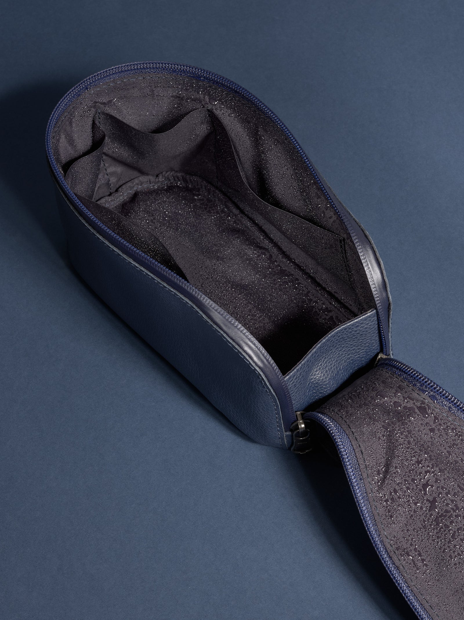 Top-down view of the empty, open navy leather toiletry bag, showing the water-resistant lining.