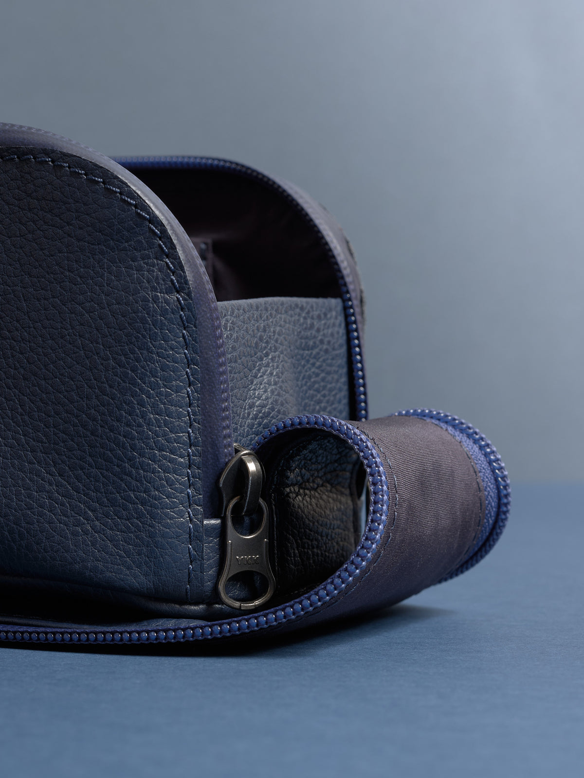 Detail shot of the navy Capra leather toiletry bag's zipper pull and textured leather material.