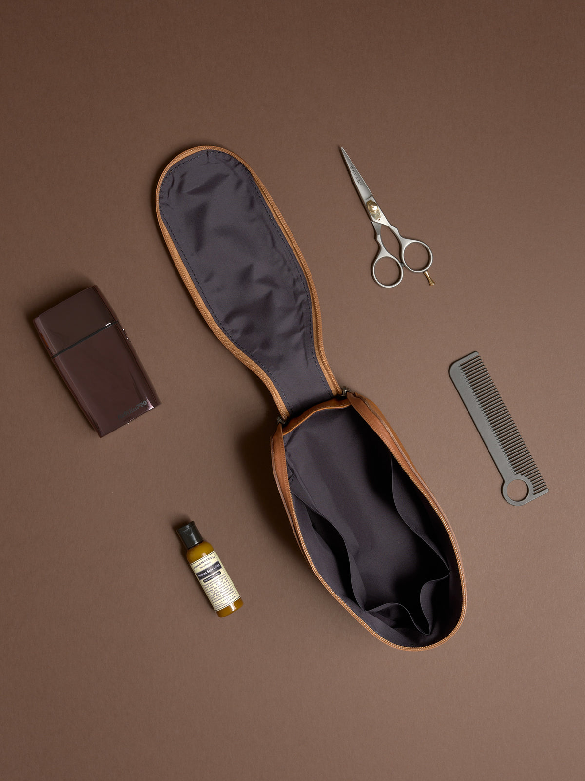 Open tan Capra Leather Toiletry Bag displayed flat with scissors, comb, and grooming products.