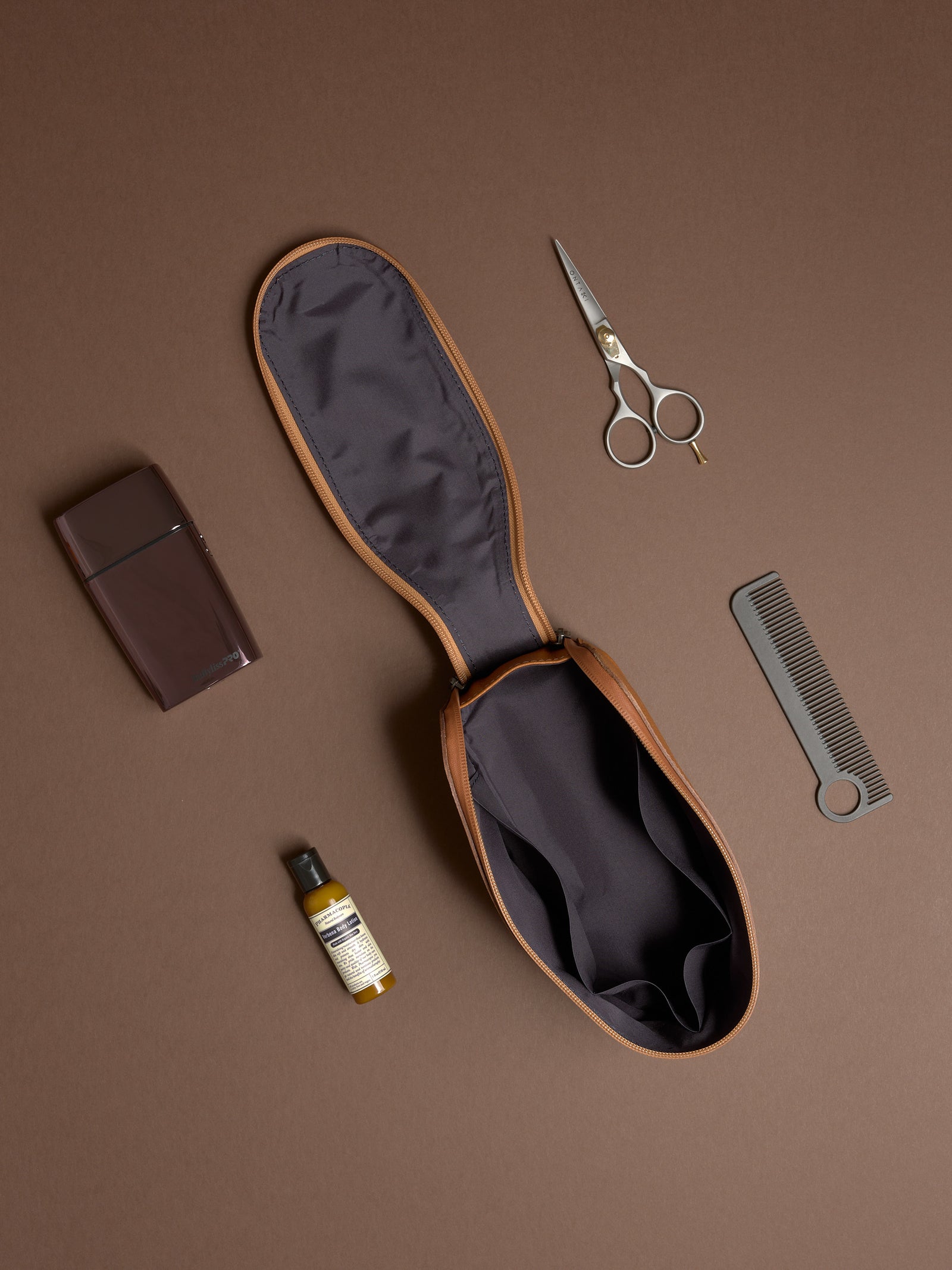 Open tan Capra Leather Toiletry Bag displayed flat with scissors, comb, and grooming products.