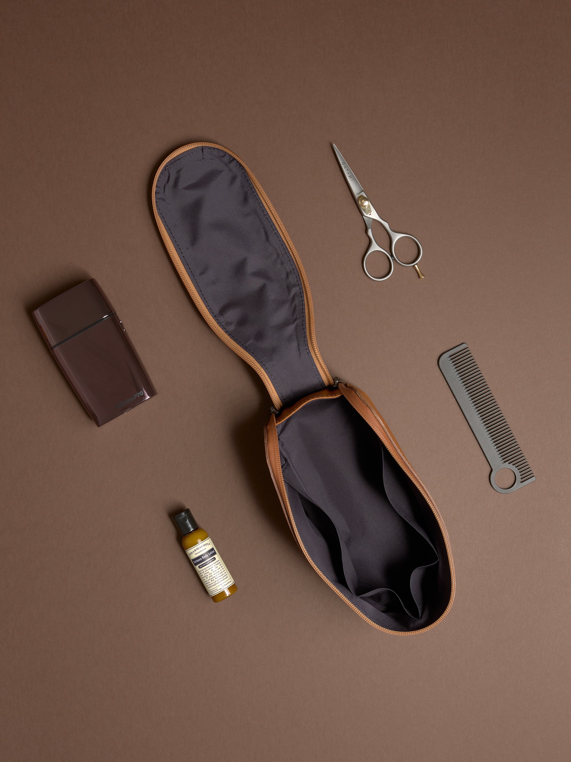 Open tan Capra Leather Toiletry Bag displayed flat with scissors, comb, and grooming products.