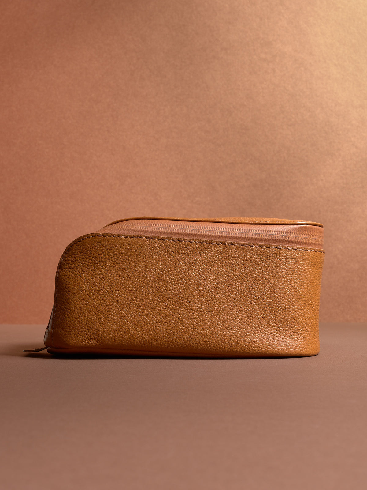 Side view of the closed tan Capra Leather Scout Toiletry Bag, showing its contoured top.