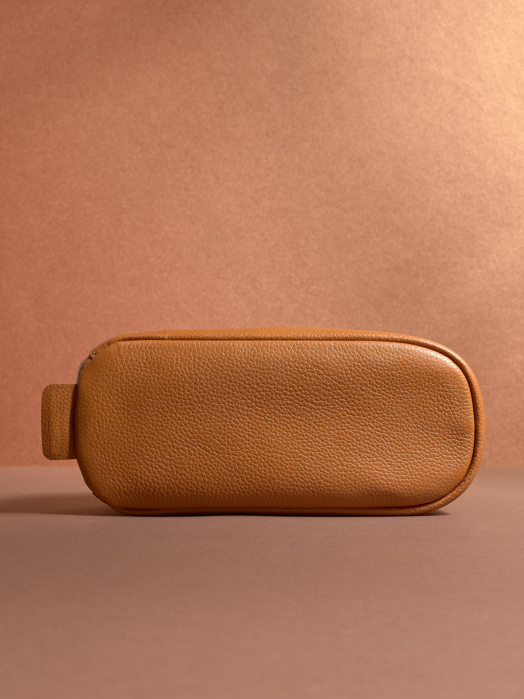 Bottom view of the tan Capra Leather Toiletry Bag with its rounded edges and carrying loop.