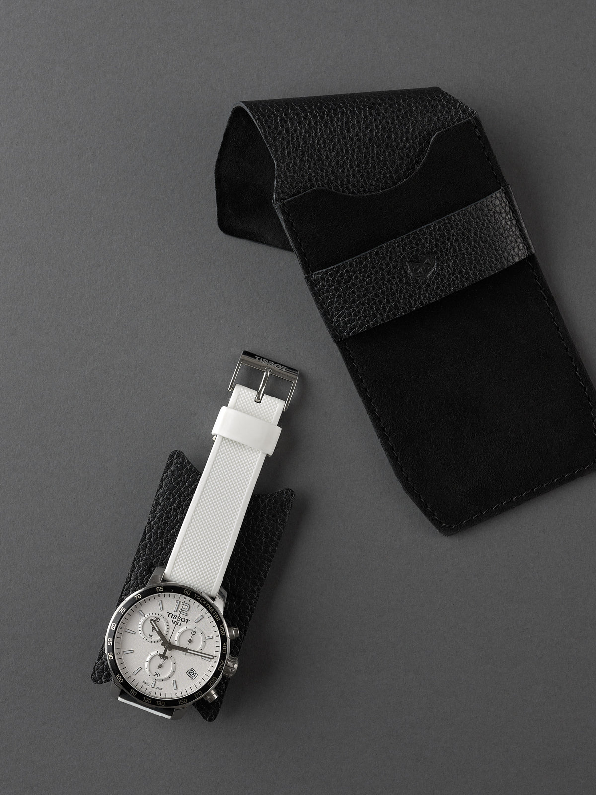Men's white strap watch on a small black leather insert with a Capra Leather watch pouch in the foreground.