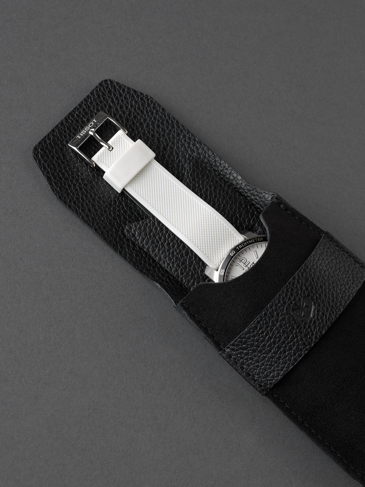 White strap chronograph watch partially inserted into a black suede watch pouch by Capra Leather.