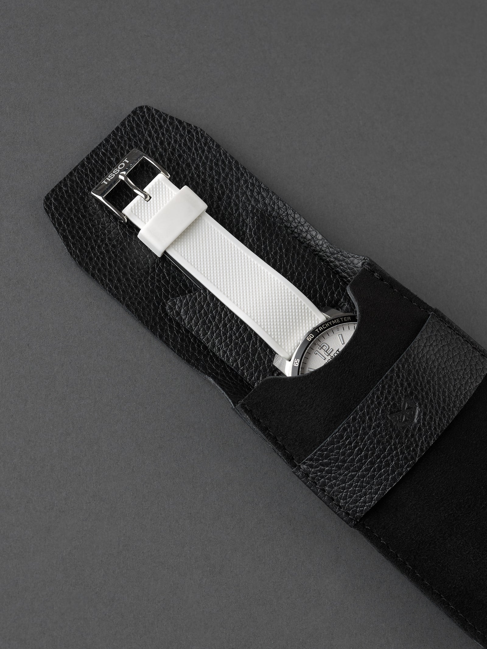 White strap chronograph watch partially inserted into a black suede watch pouch by Capra Leather.