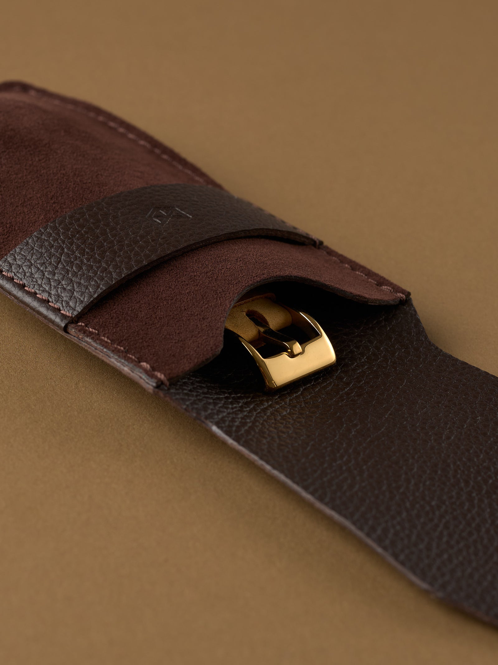 Close-up view of a gold watch buckle securely tucked behind the textured leather closure of the Suede Watch Pouch.