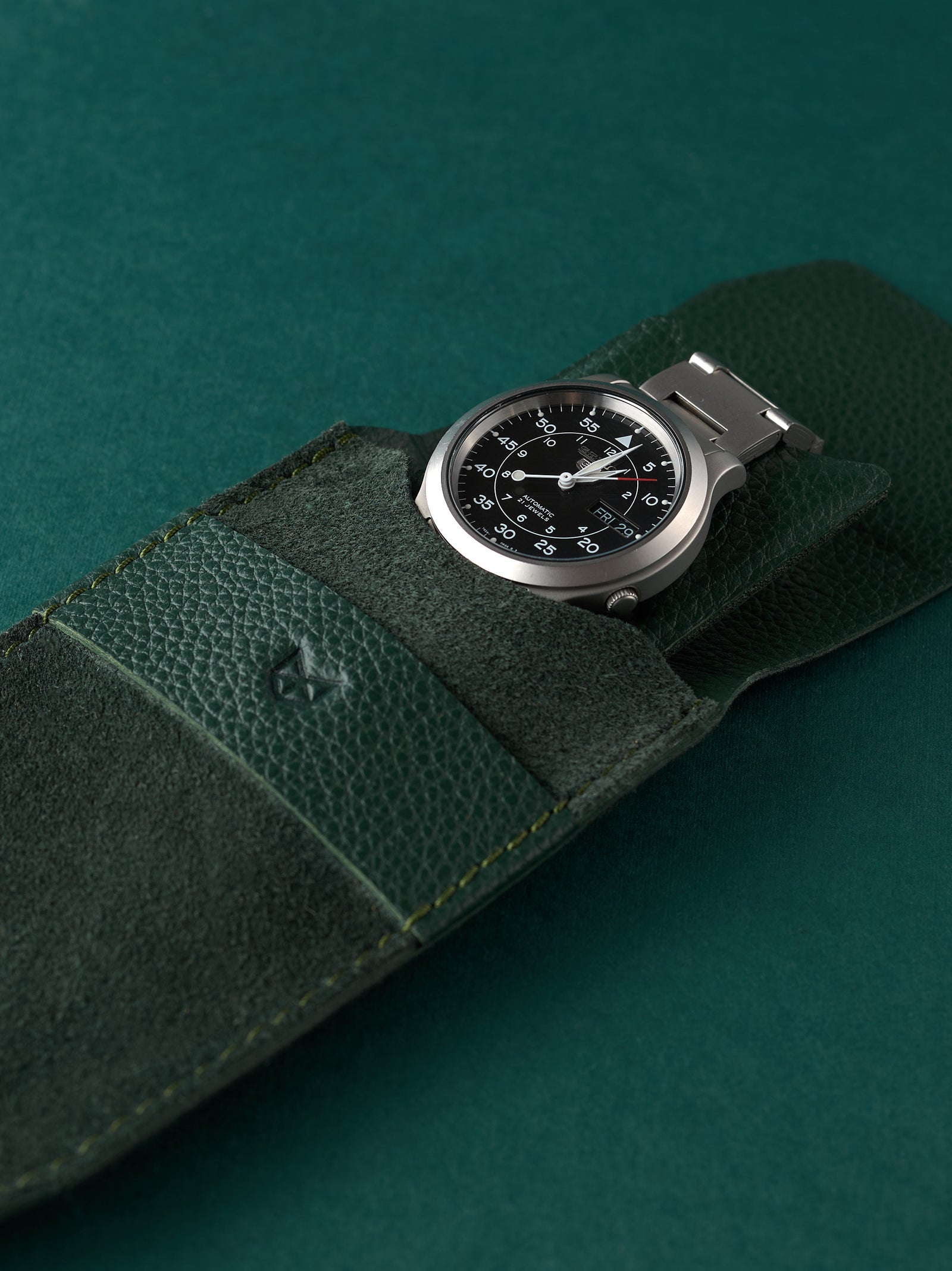 Stainless steel automatic watch tucked into a green suede watch pouch by Capra Leather.