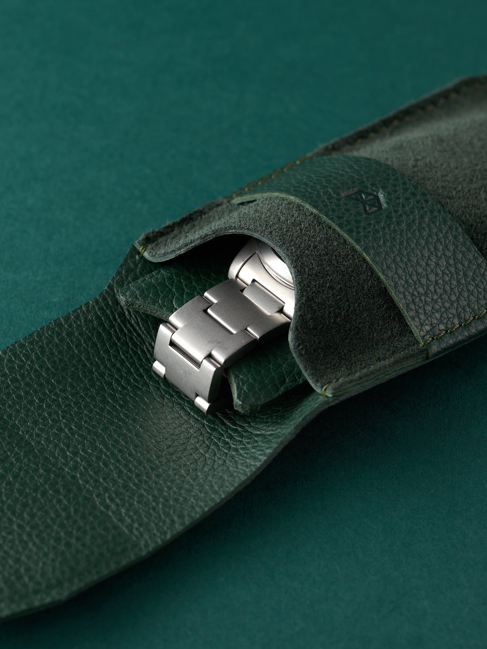 Stainless steel automatic watch tucked into a green suede watch pouch by Capra Leather.