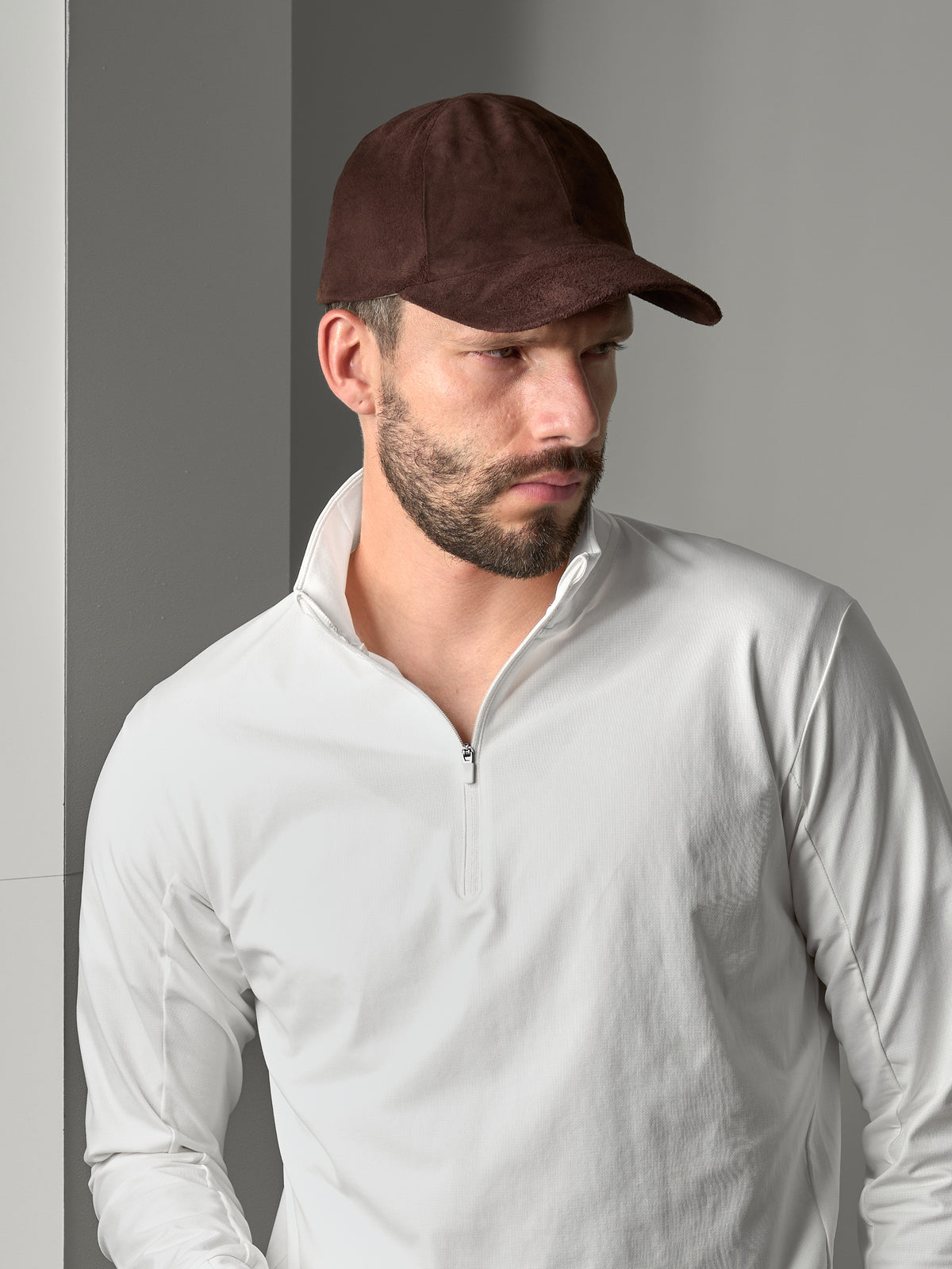 A man wearing a green suede cap and a dark grey sweatshirt, pulling the cap down to obscure his face.