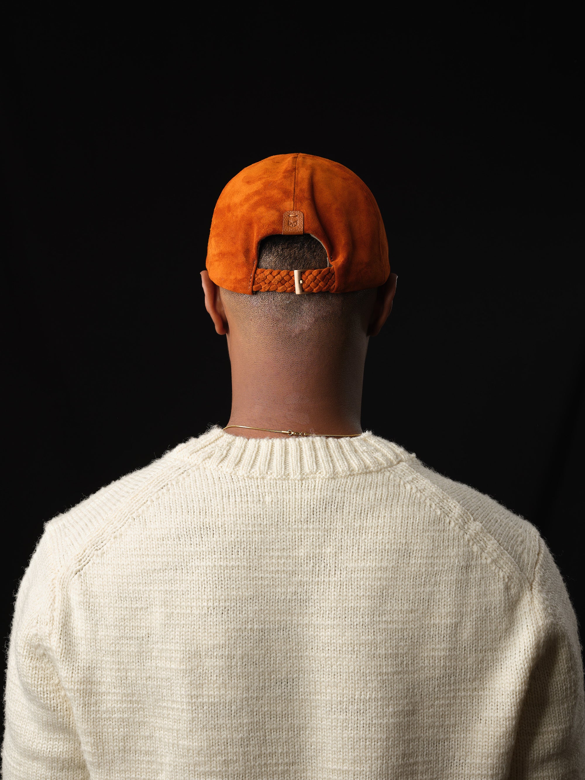 Back view of a tan suede baseball cap with braided strap and buckle, handcrafted by Capra Leather