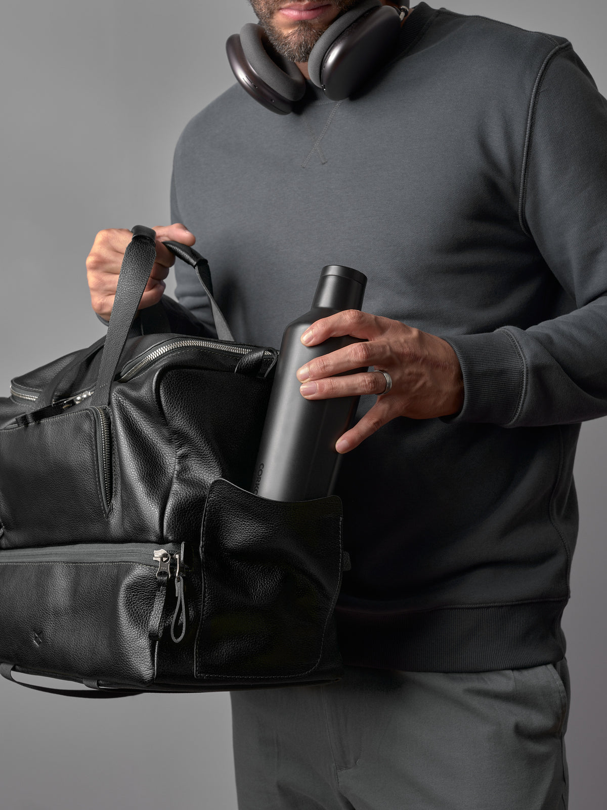 A man puts a black water bottle into the side pocket of the black leather Capra duffel bag.