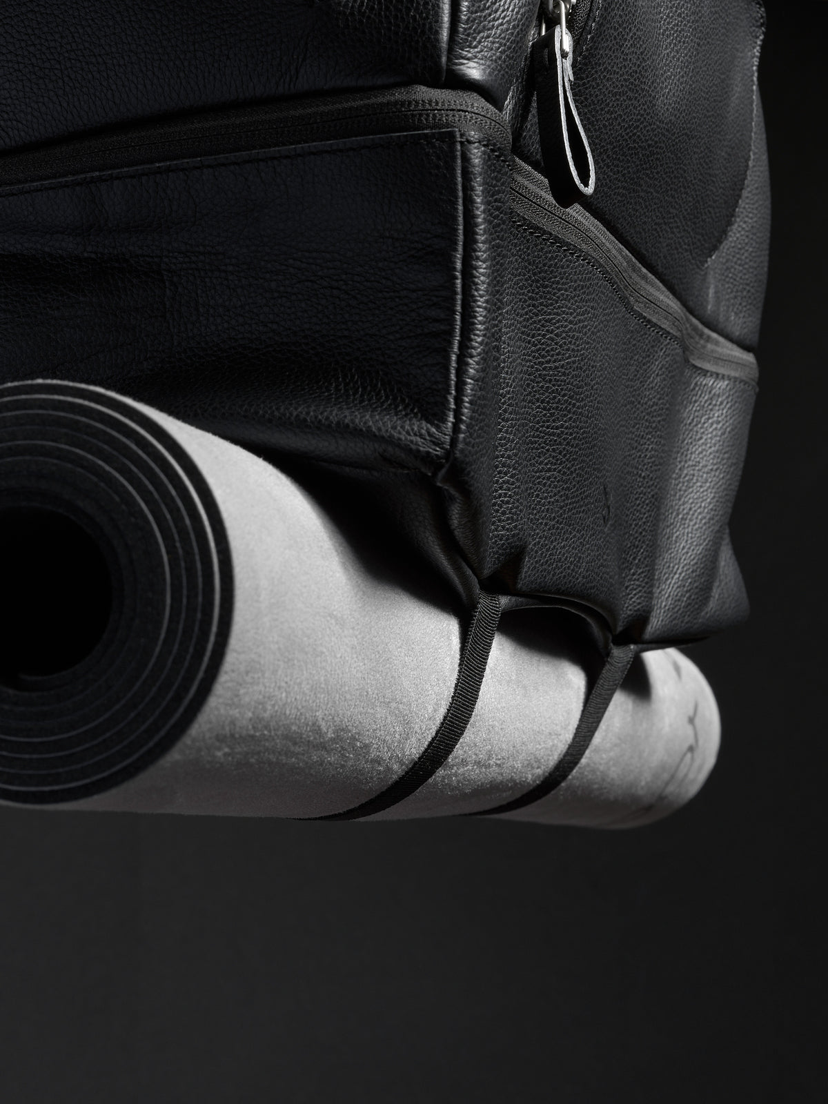 Close-up of the black leather travel bag with a rolled yoga mat attached to the bottom.