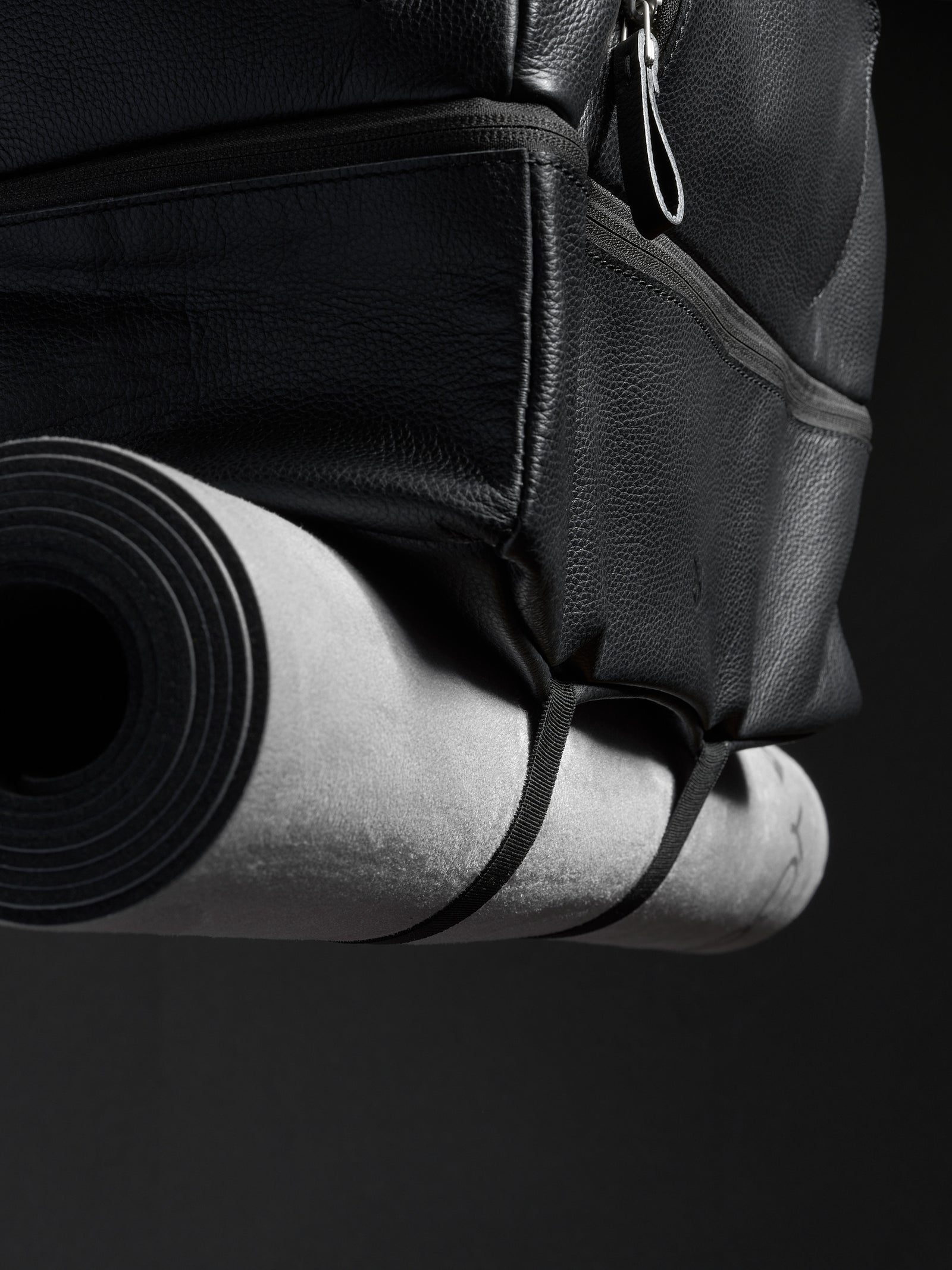 Close-up of the black leather travel bag with a rolled yoga mat attached to the bottom.