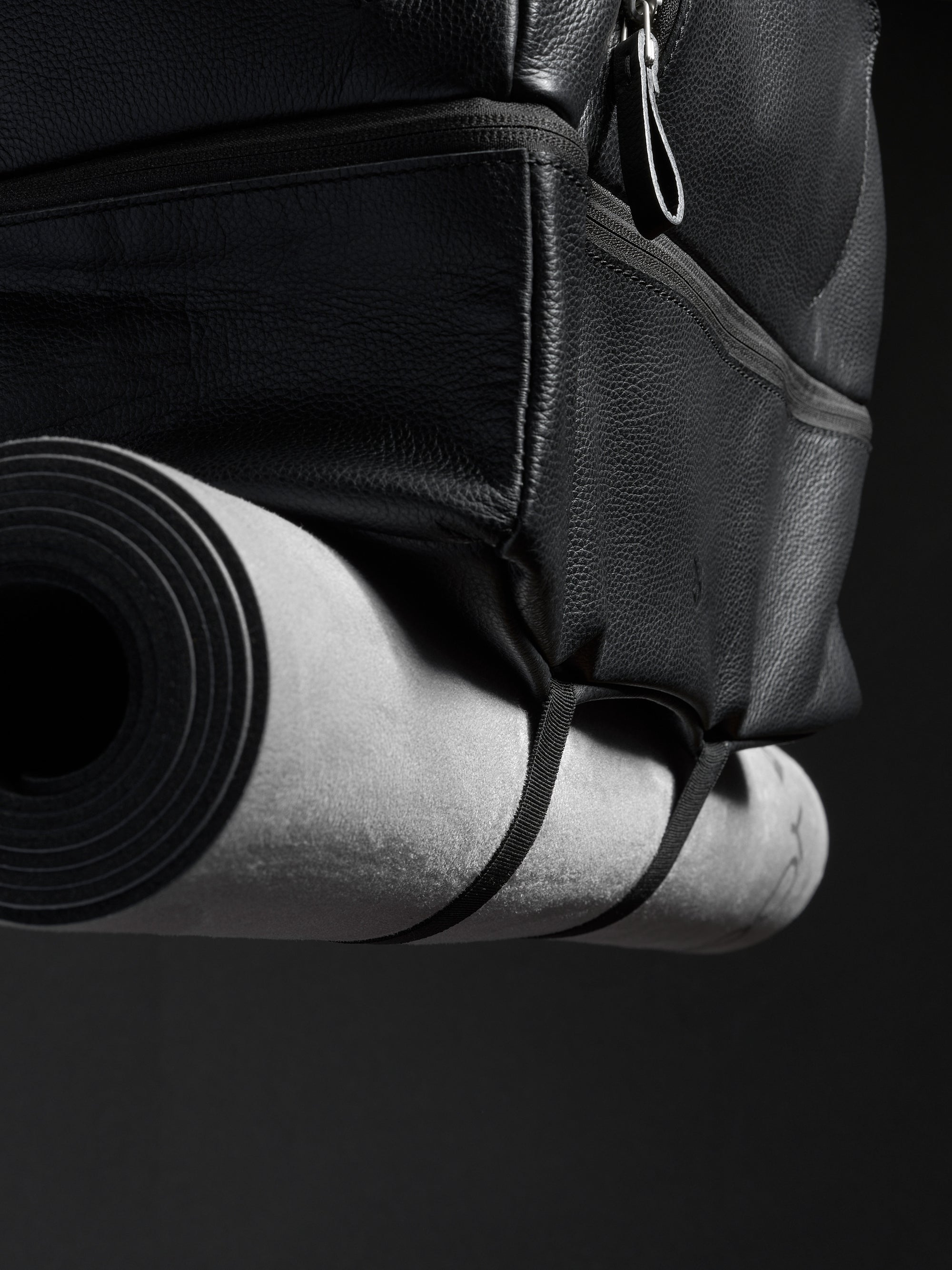 Close-up of the black leather travel bag with a rolled yoga mat attached to the bottom.