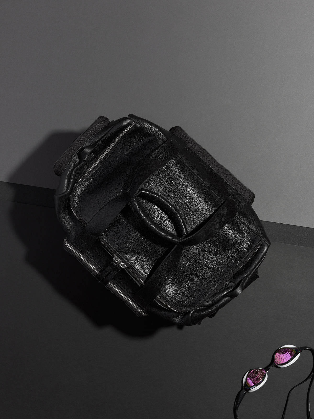 Black leather duffel bag shot from above with sunglasses and swimming gear, showing its durable, waterproof design.