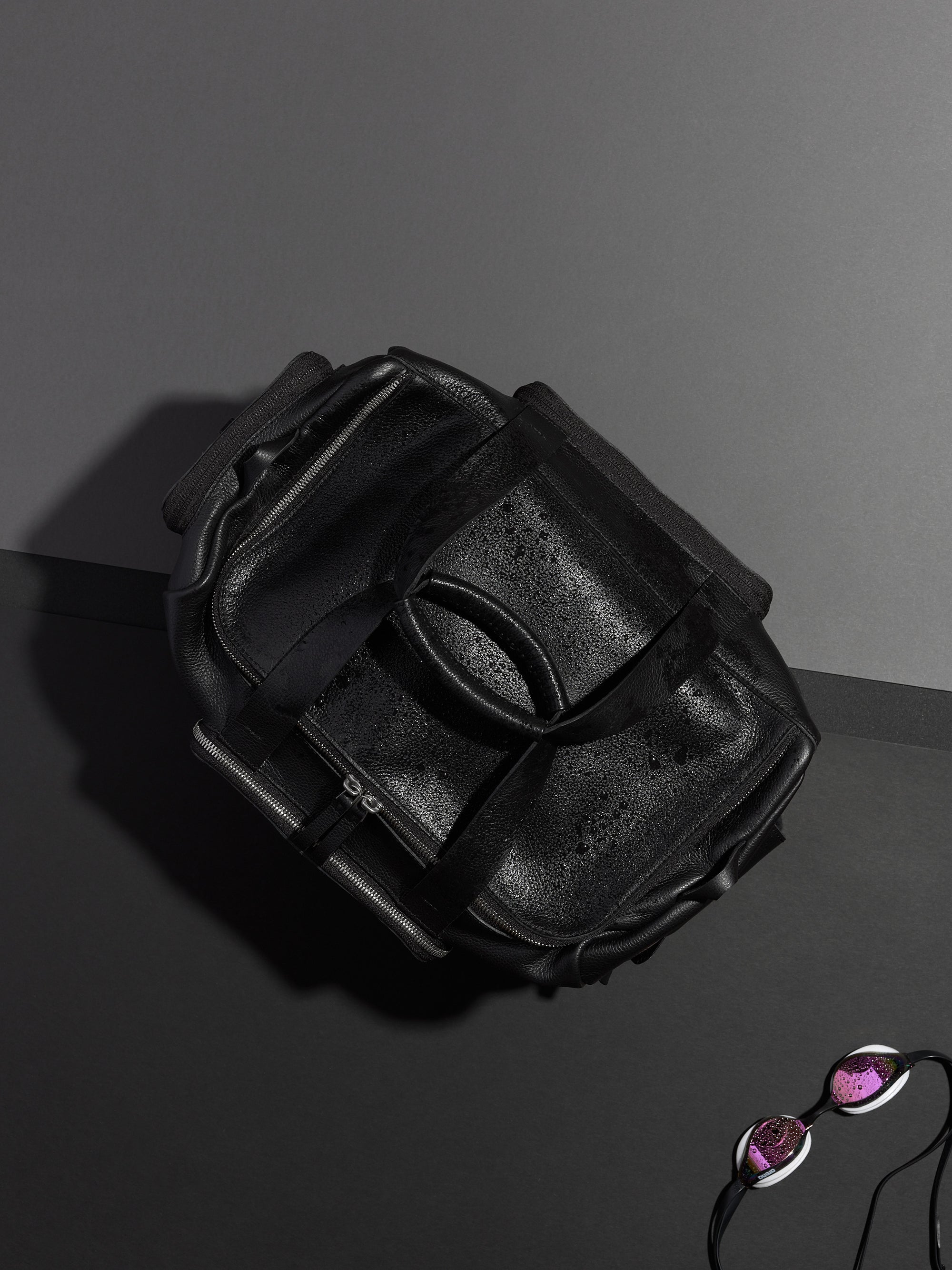 Black leather duffel bag shot from above with sunglasses and swimming gear, showing its durable, waterproof design.