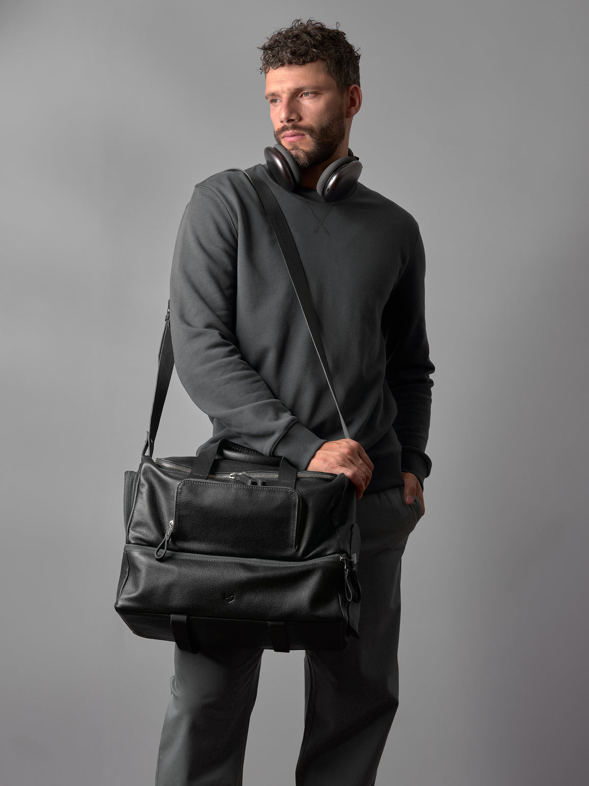 A man models the black leather Ventra duffel bag, highlighting its stylish design and comfortable shoulder strap.