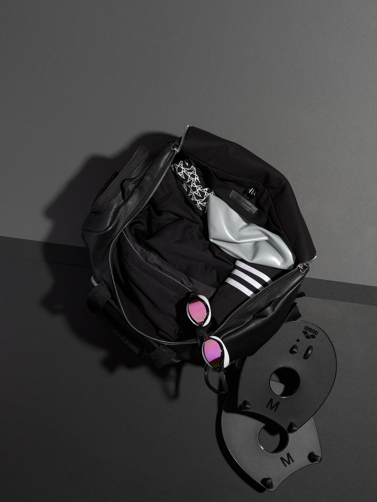 Capra Leather duffel bag, unzipped with gym clothes, socks, and swim paddles inside