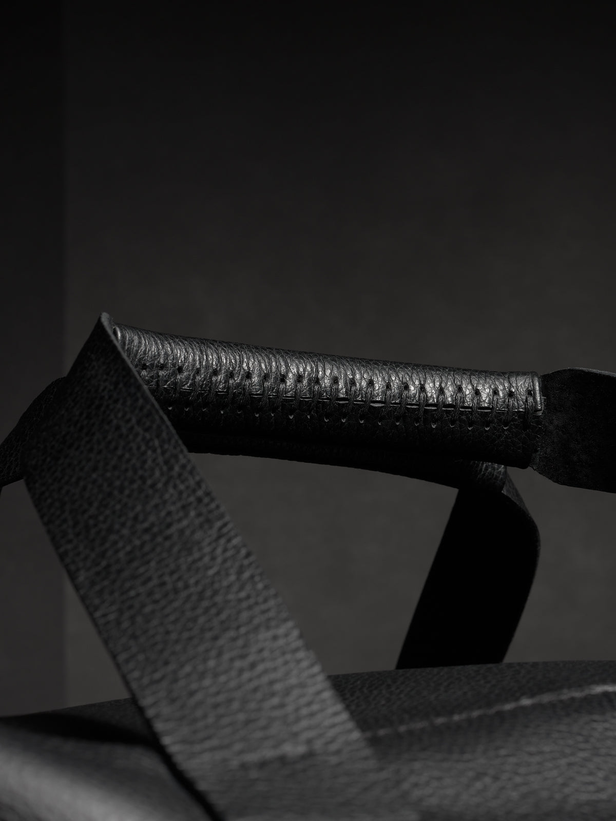 Close-up of the black leather handle of the Ventra duffel, highlighting the detailed stitching and pebbled texture.