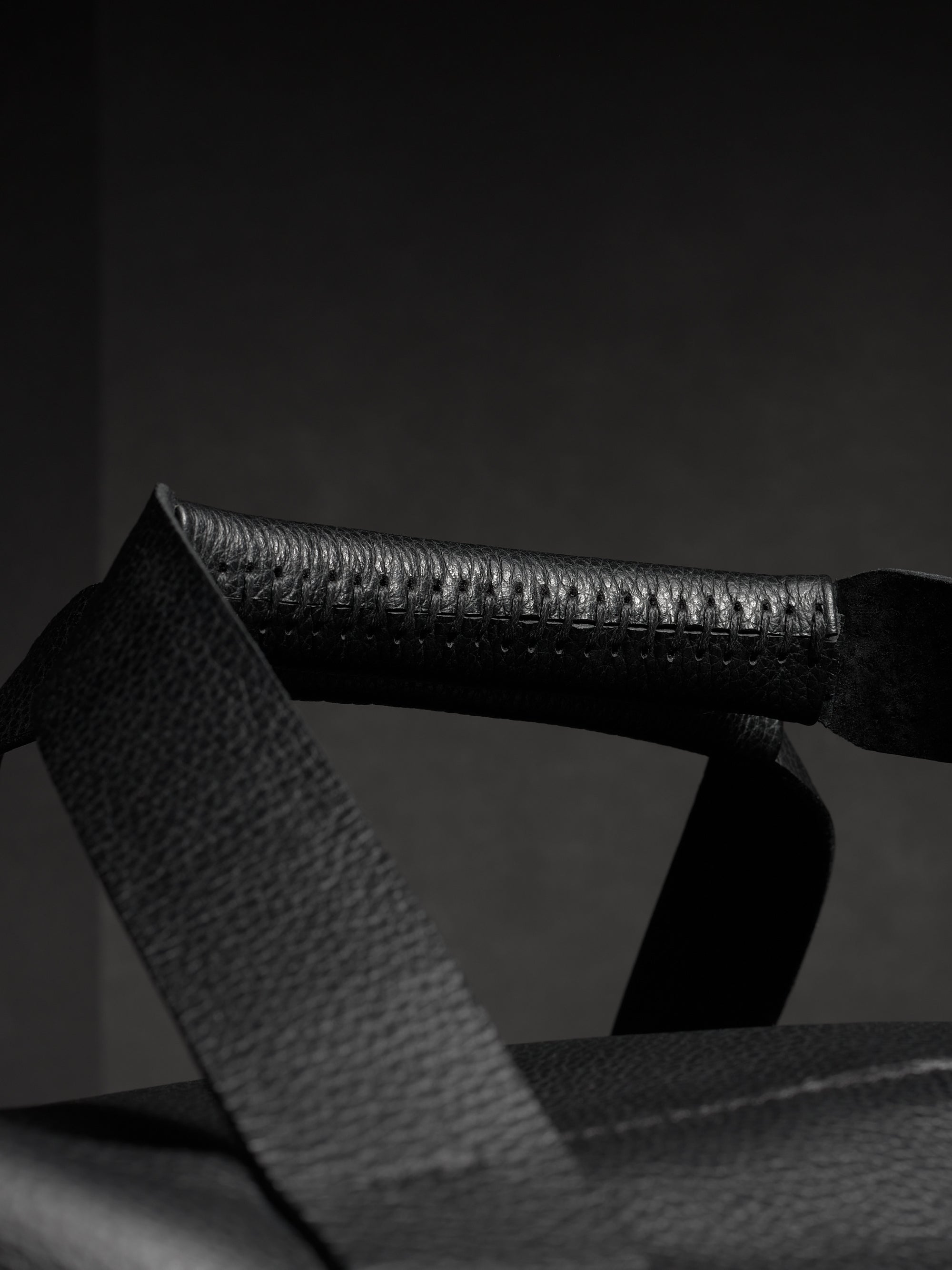 Close-up of the black leather handle of the Ventra duffel, highlighting the detailed stitching and pebbled texture.