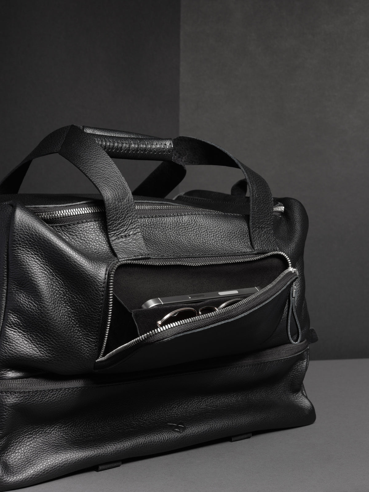 Close-up of the side pocket of the black leather duffel, with a phone and sunglasses inside.