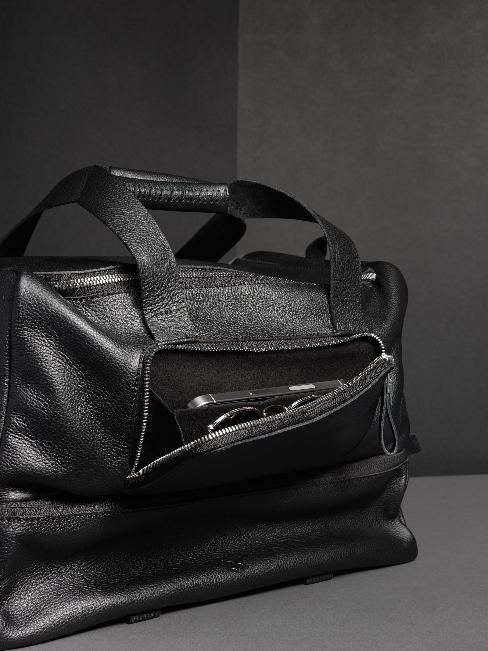 Close-up of the side pocket of the black leather duffel, with a phone and sunglasses inside.