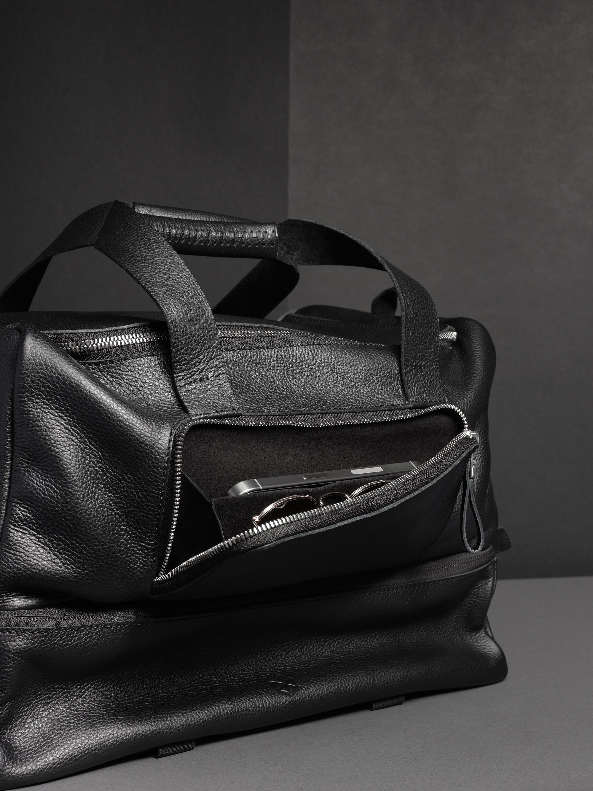 Close-up of the side pocket of the black leather duffel, with a phone and sunglasses inside.