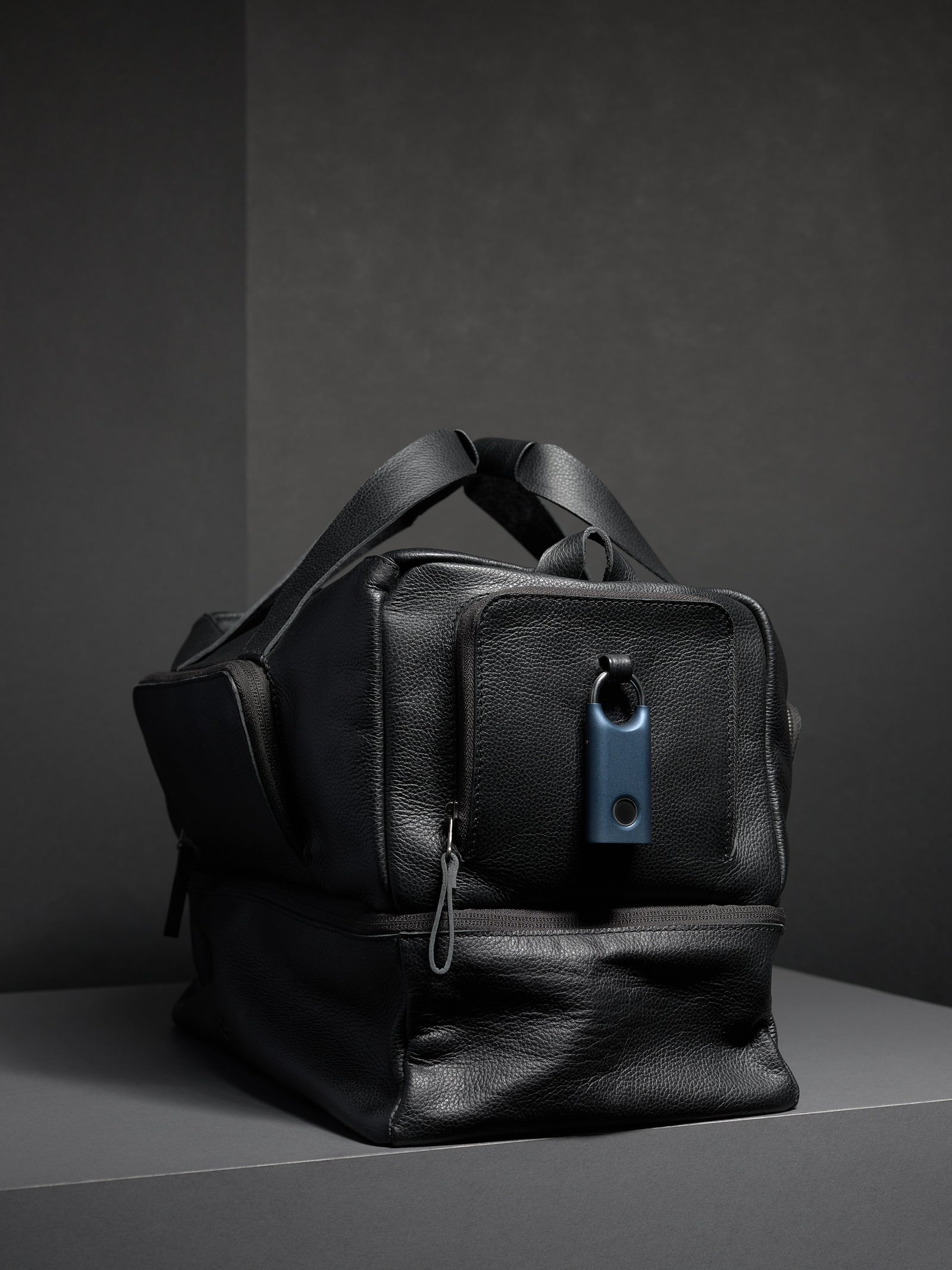 Front view of the black leather travel duffel bag with a lock on the exterior front pocket.