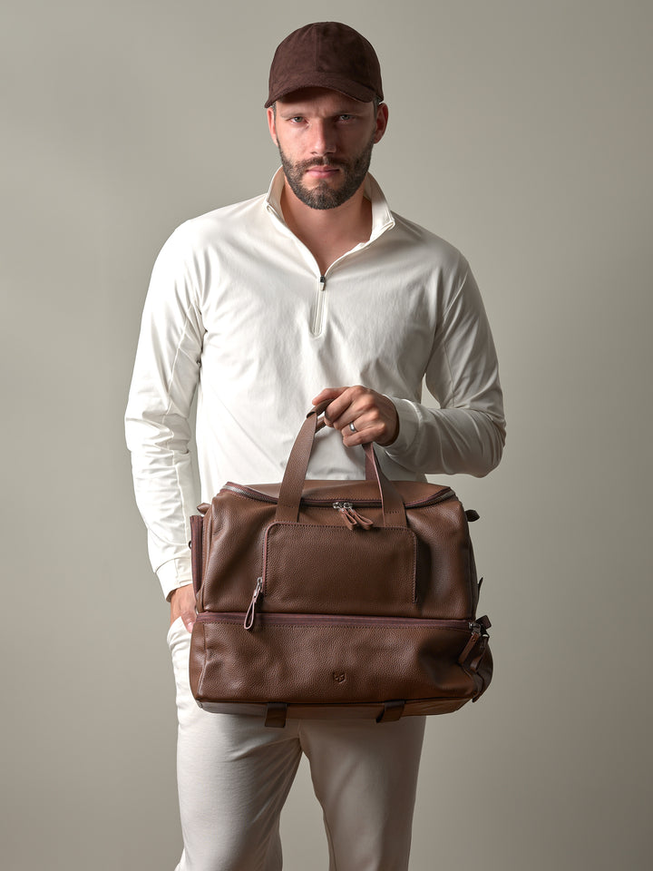A man in athletic wear holding the brown leather Ventra Holdall by its top handles, showcasing it as a luxury sports bag.