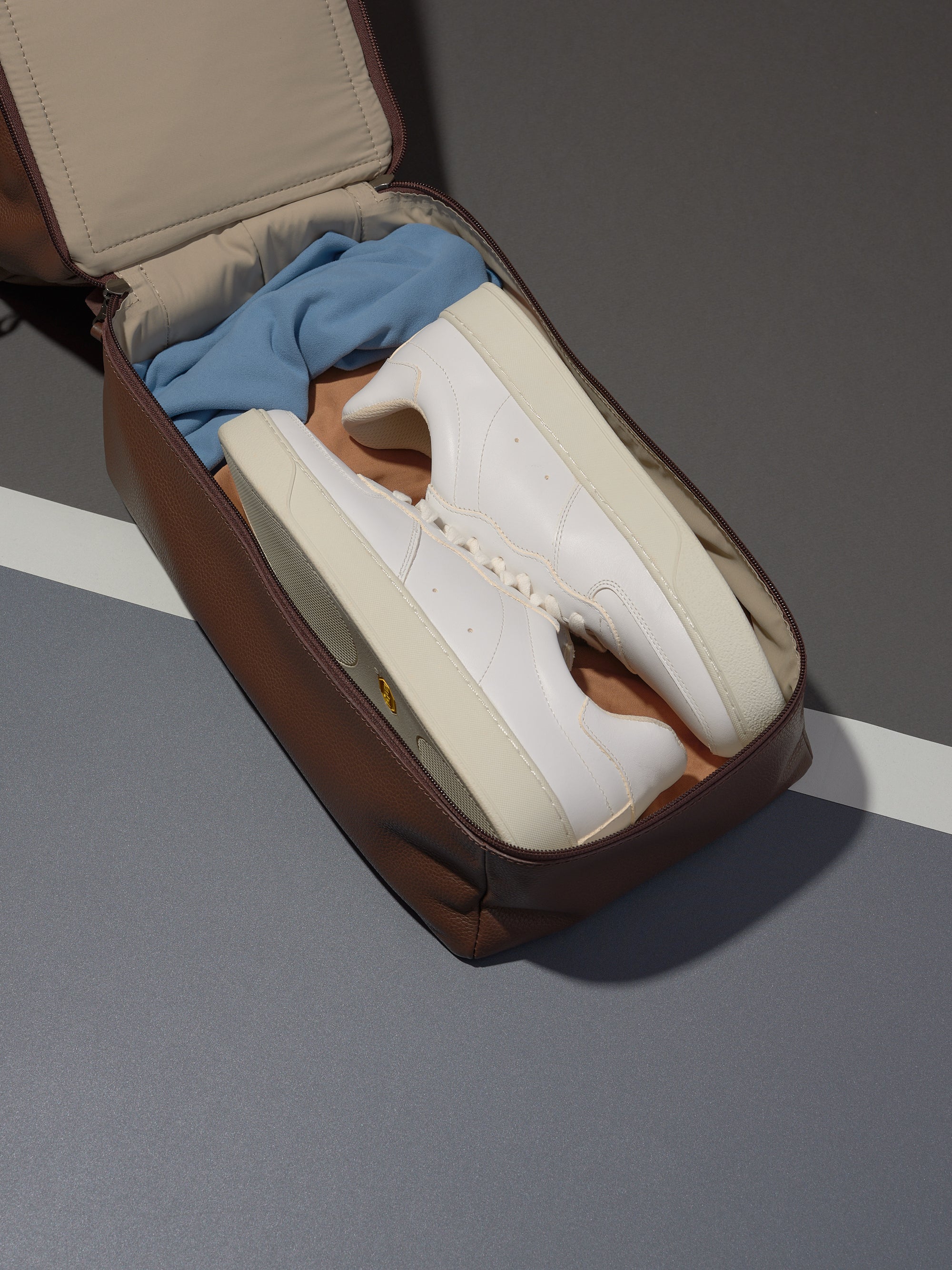 The Ventra Holdall's separate shoe compartment in brown leather, open to hold a pair of white sneakers for the gym.