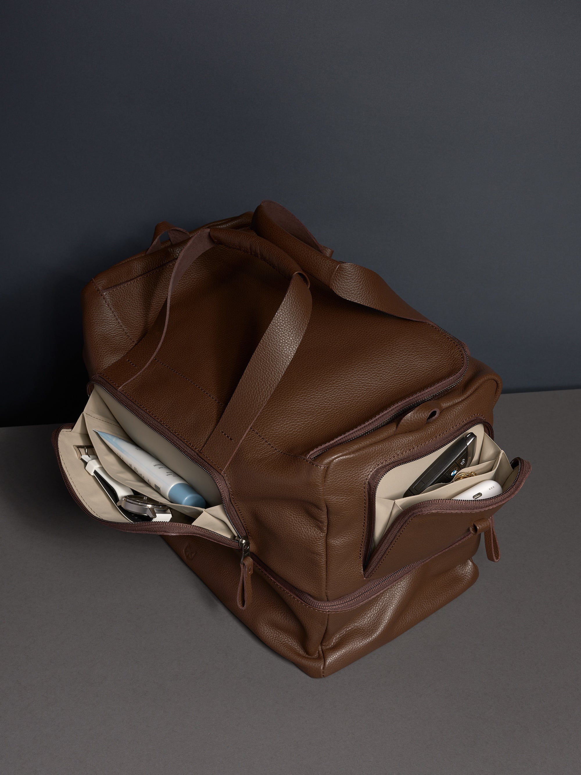 The brown leather Ventra Holdall with its side wing pockets open, displaying organized storage for toiletries.