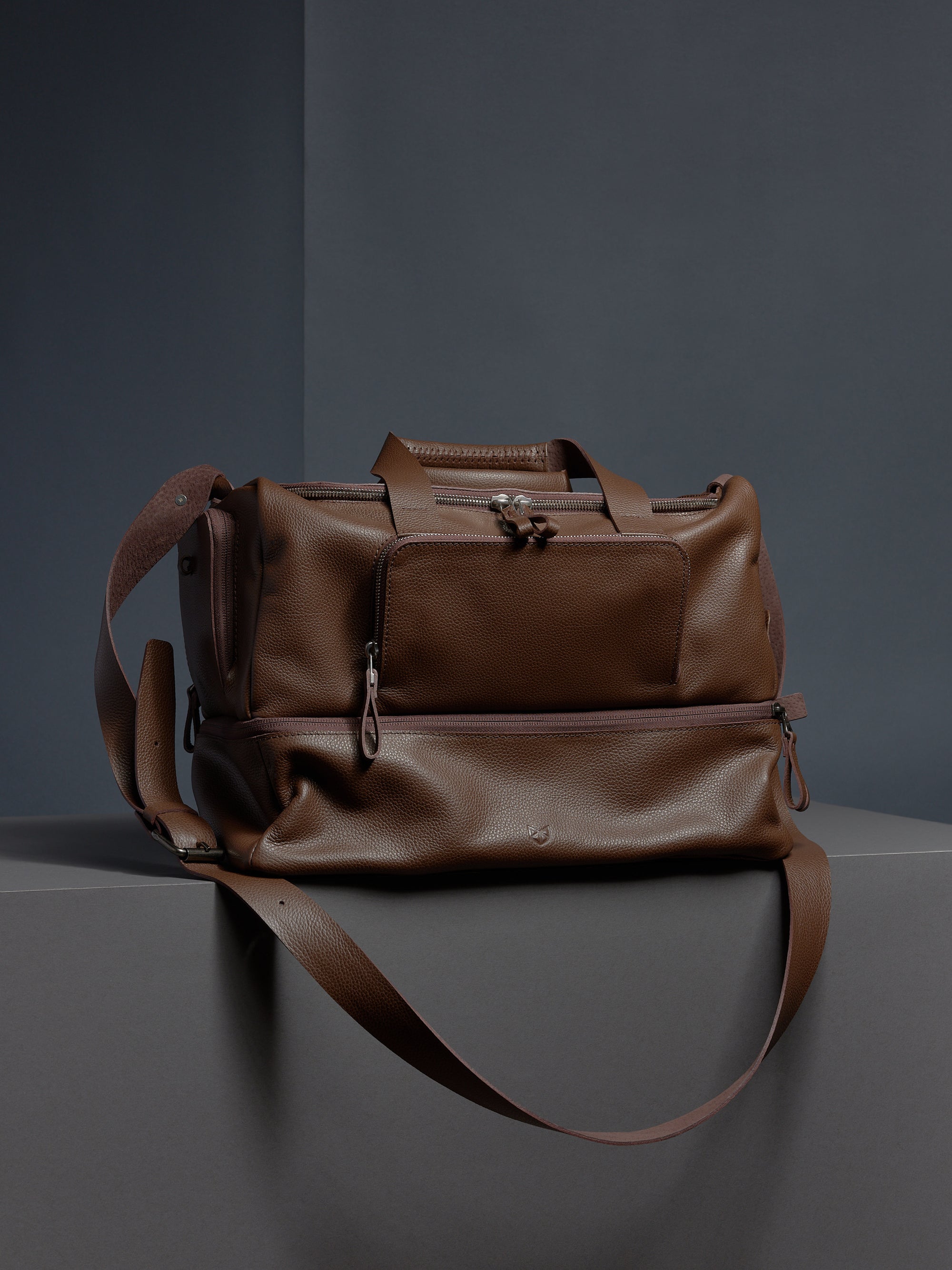 A man in athletic wear holding the brown leather Ventra Holdall by its top handles, showcasing it as a luxury sports bag.