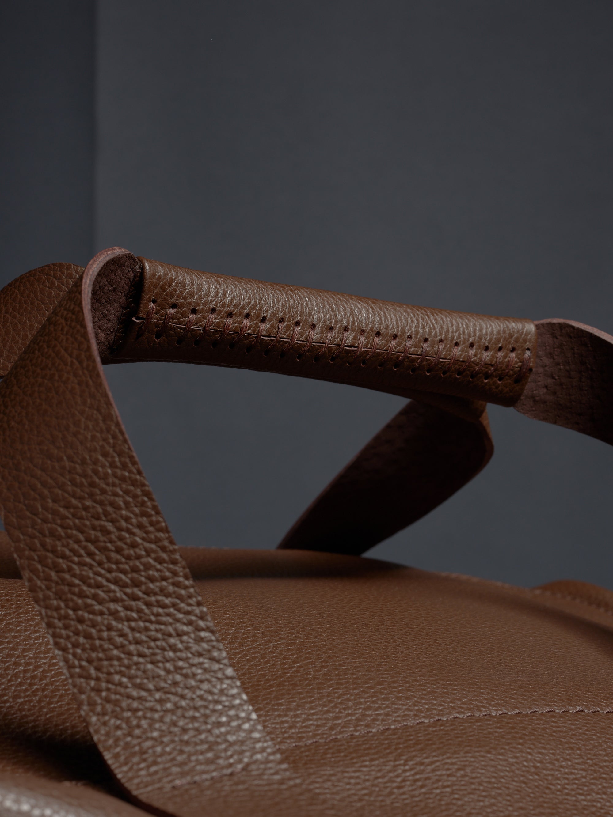 A detailed close-up of the hand-stitched handle on the brown leather Ventra Holdall, showing quality craftsmanship.