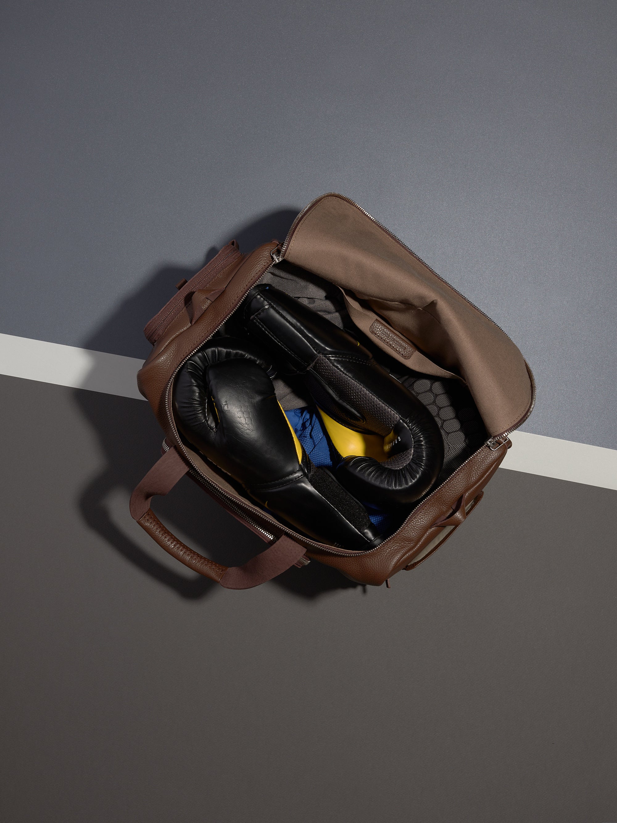 Top-down view of the open brown leather Ventra Holdall, used as a gym bag with black boxing gloves packed inside.