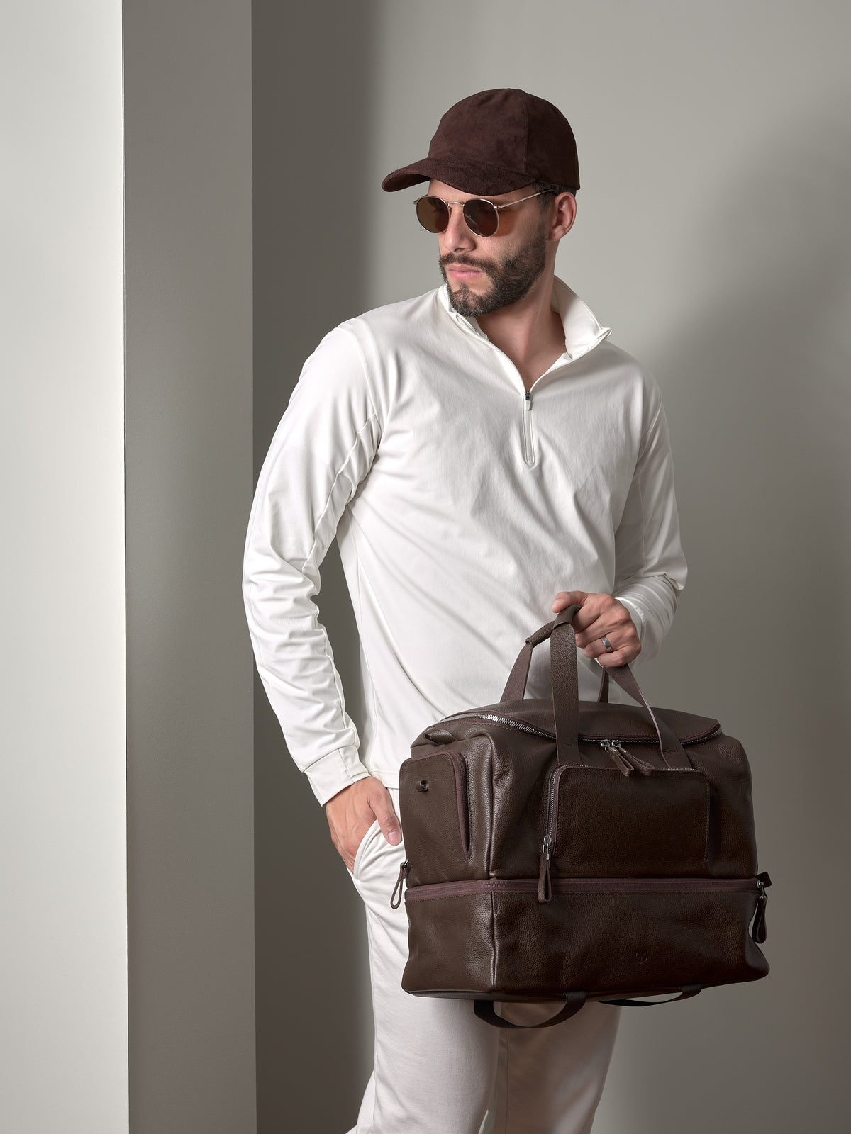 A man with sunglasses and a cap holding the dark brown Capra Leather Ventra Holdall, a luxurious travel bag.
