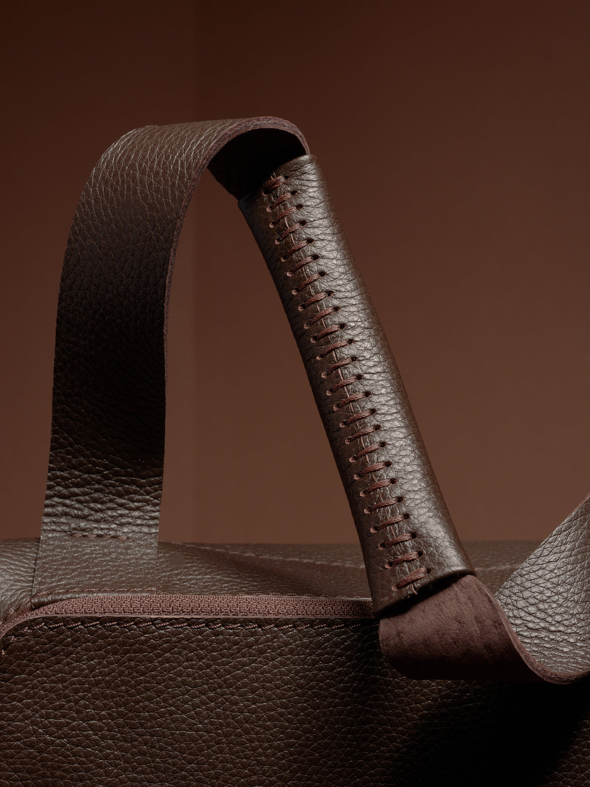 Close-up of the Ventra Holdall's handle, showcasing hand-stitched leather detail.