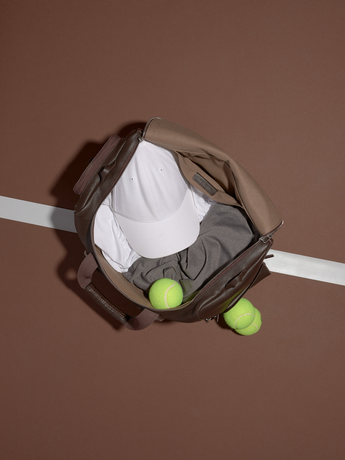 A Ventra Holdall bag opened from the top, holding a white hat and grey shirt with two tennis balls next to it.