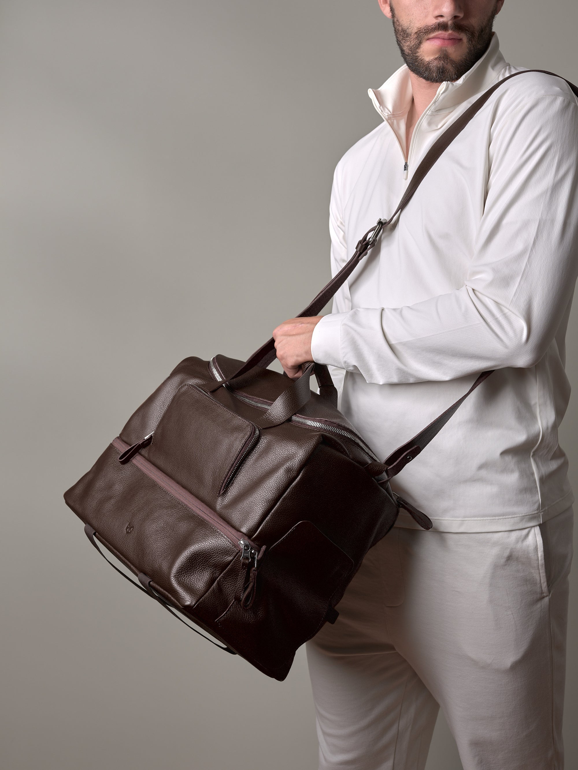 A close-up of a man wearing a white shirt and holding the dark brown leather Ventra Holdall with its shoulder strap.